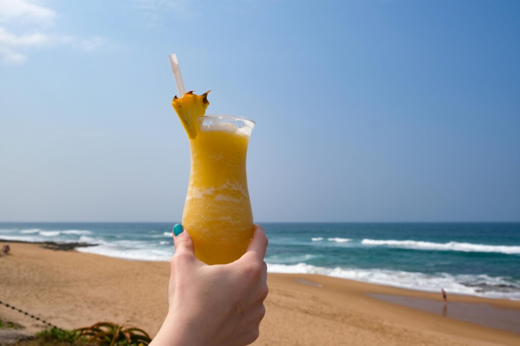 Refreshing pineapple cocktail held by a beach with ocean view.